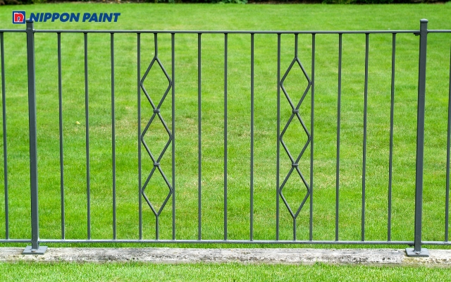 Cổng sắt xanh đậm cách điệu hòa cùng sắc xanh cây cối, tạo tổng thể hài hòa và cuốn hút cho ngôi nhà